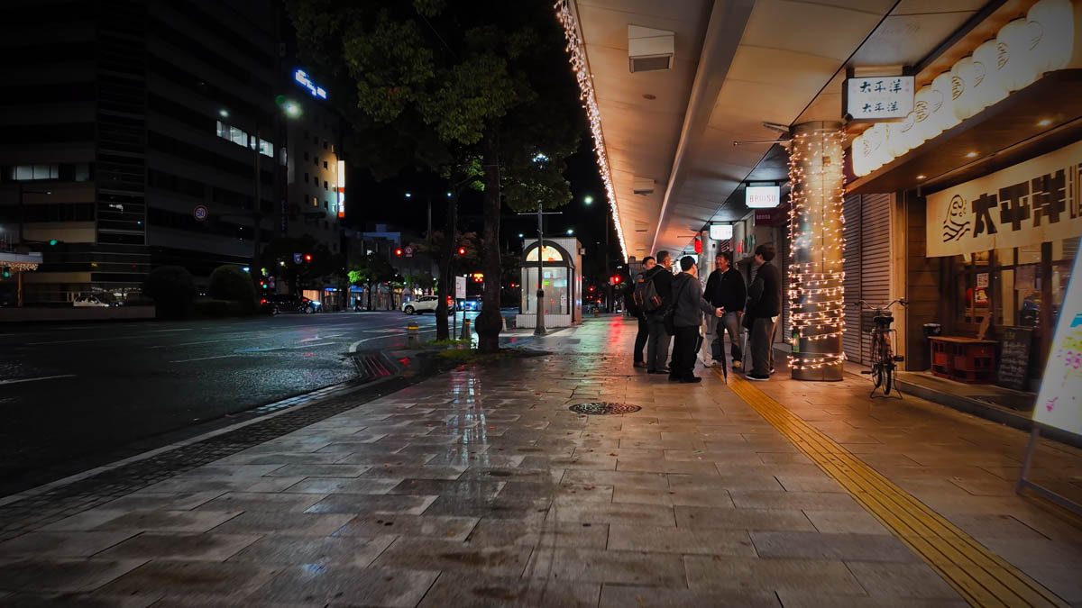 People walking along Keyaki-dori at night, a group of revellers in the mix