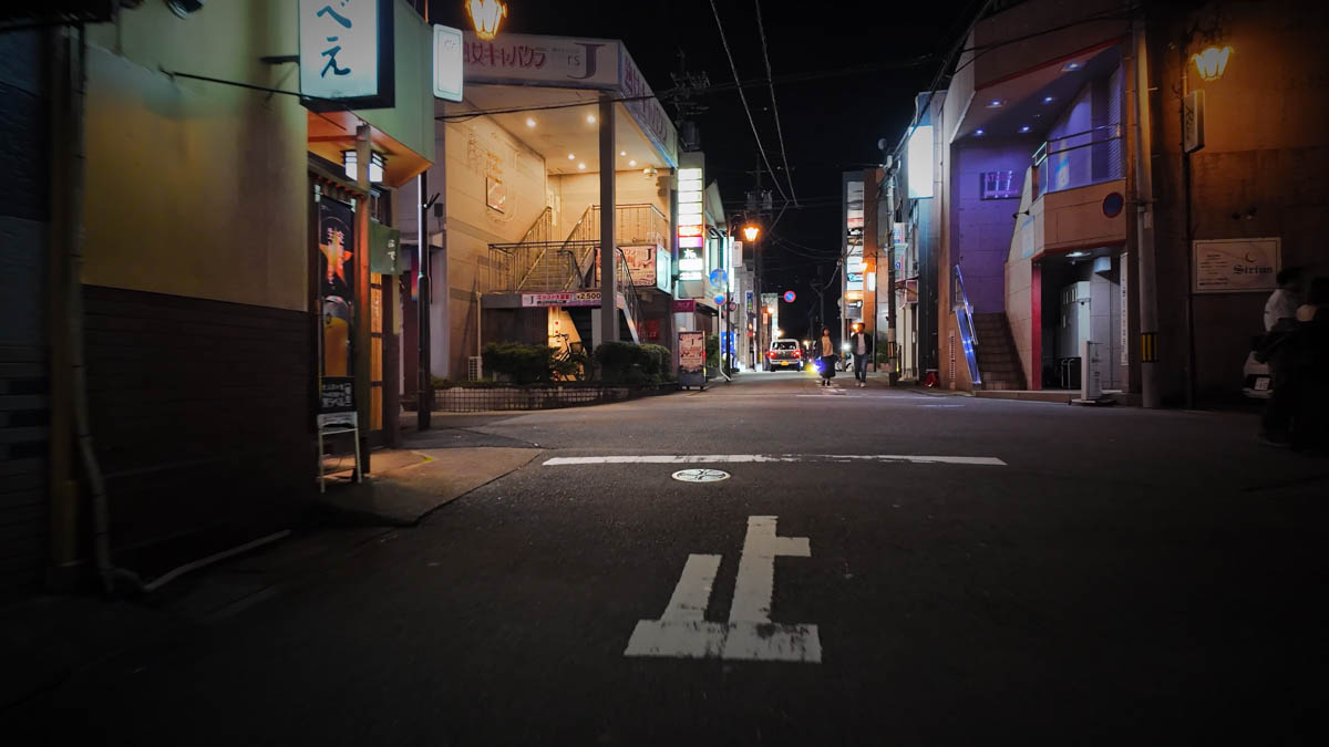A quiet night street in the bar district, a few people walking through