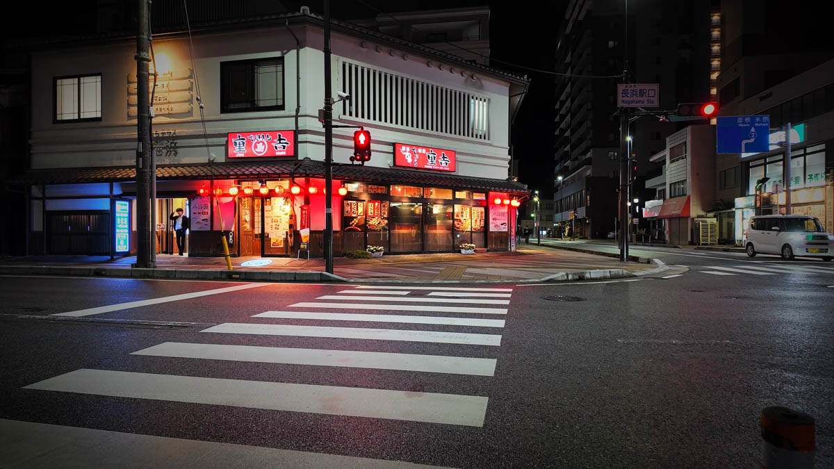 A yakitori restaurant near the station front, its warm interior light and noren curtain visible