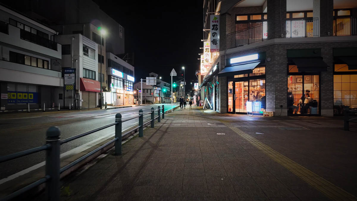 The well-lit station front street at night, restaurants and streetlamps lining the road