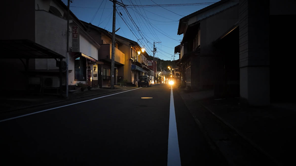 Dusk descending fast in the mountain town The mountain town sliding rapidly into night, buildings beginning to silhouette against the fading sky