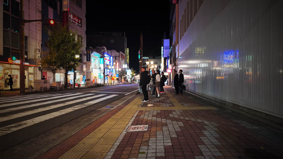 Office workers and students waiting at a crosswalk near the station during the evening rush