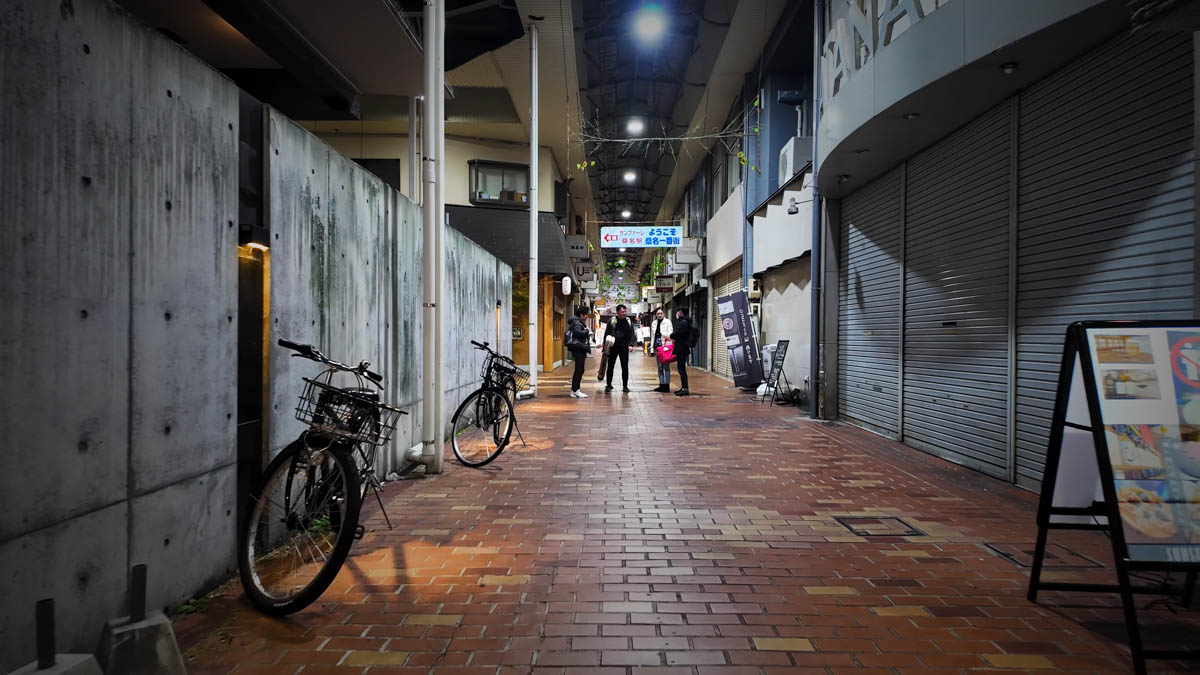 A retro covered shopping arcade near the station. Many shutters are down on a Sunday night