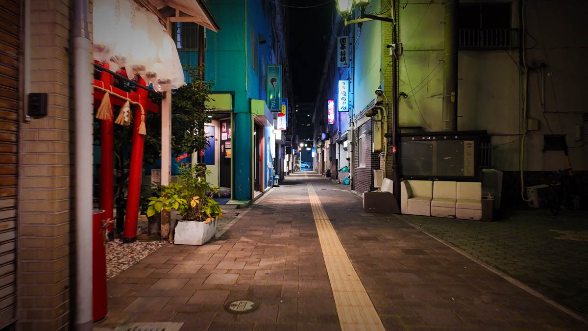 A dimly lit back alley with izakayas and snack bars, their signs glowing softly