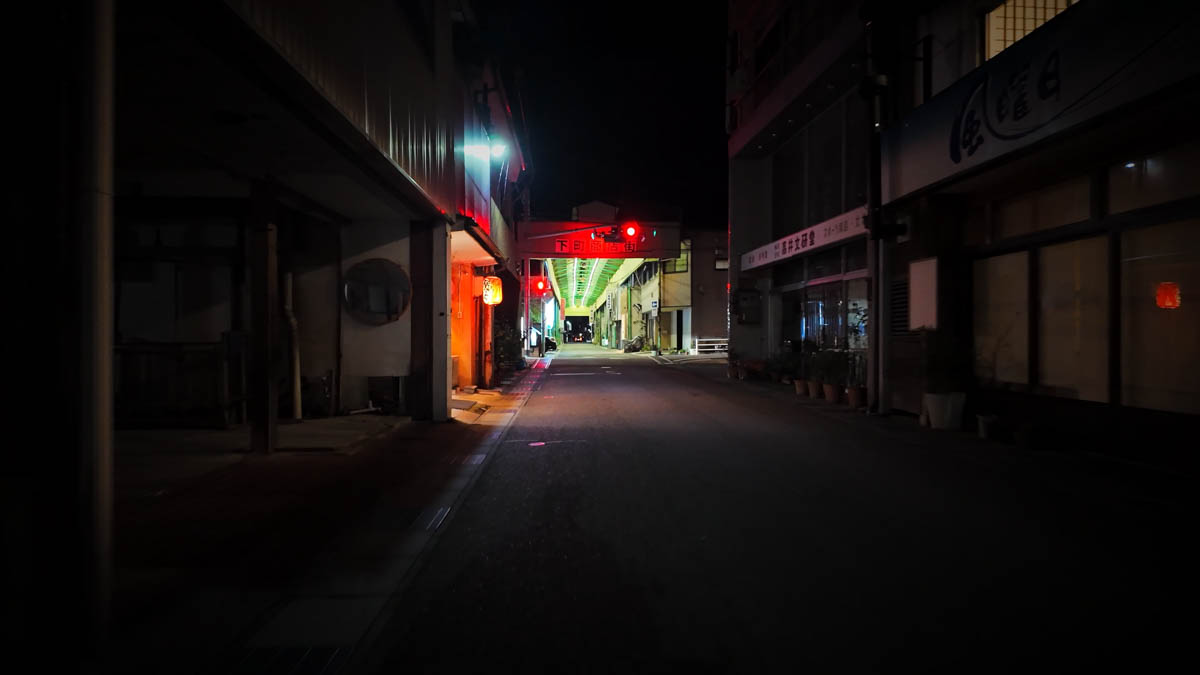 The entrance to Shimomachi Shopping Street seen beyond a red traffic light and small lanterns