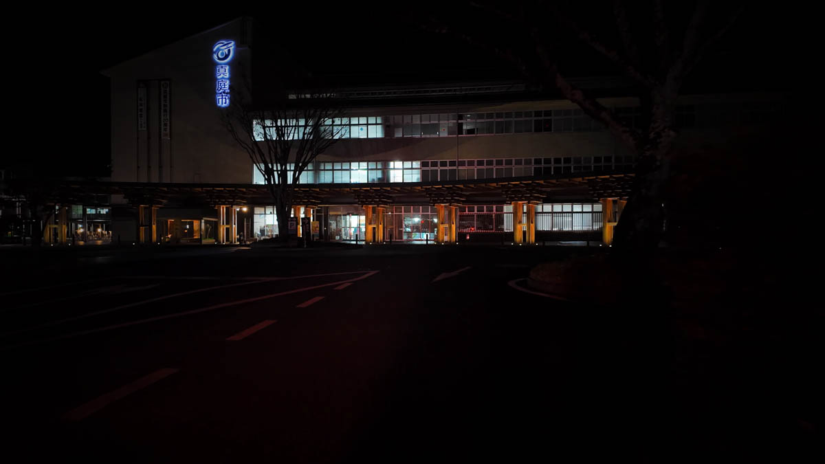 Maniwa City Hall at night, with the blue Maniwa logo glowing near the top of the building