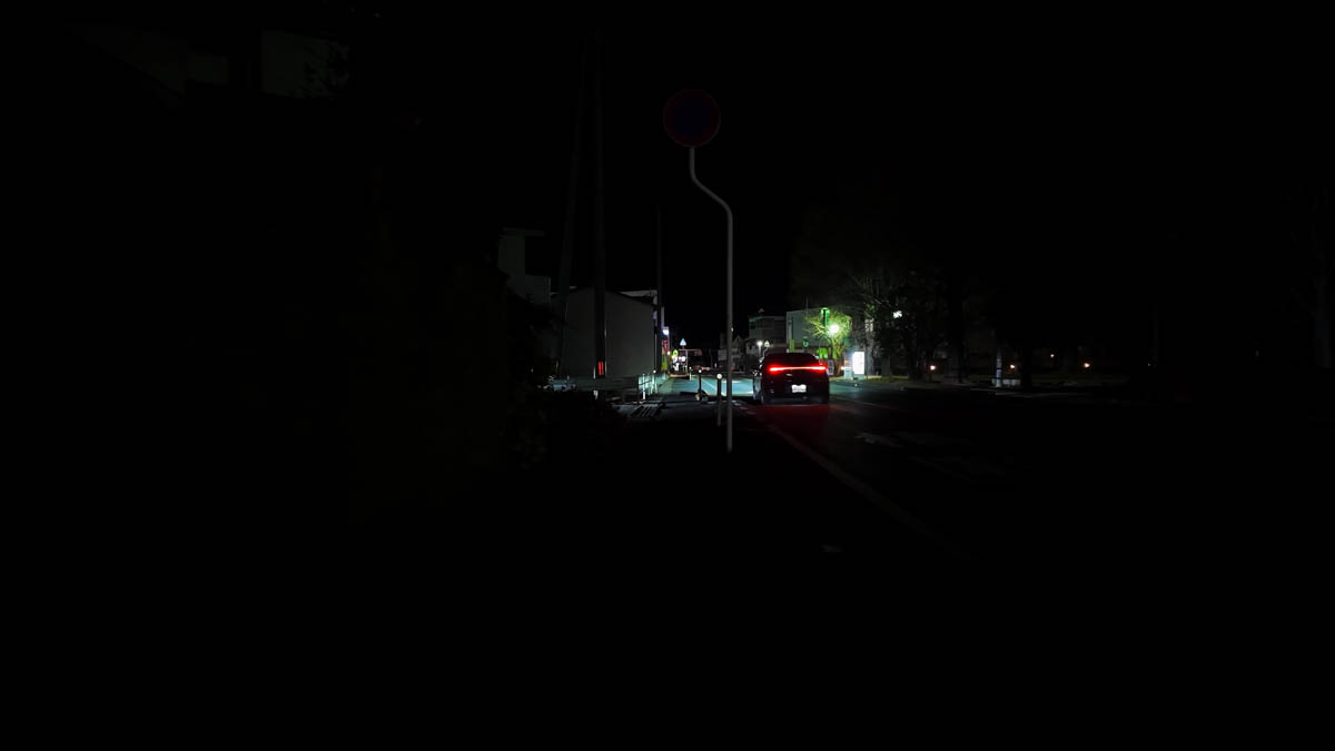 A dark night intersection, with the red tail lights of a car ahead
