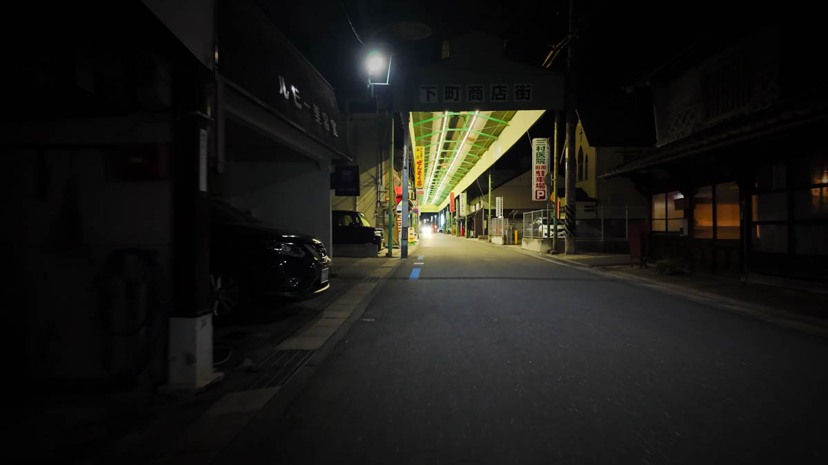 Exterior view of the Shimomachi Shopping Street entrance, with a green roof and a sign reading Shimomachi Shopping Street