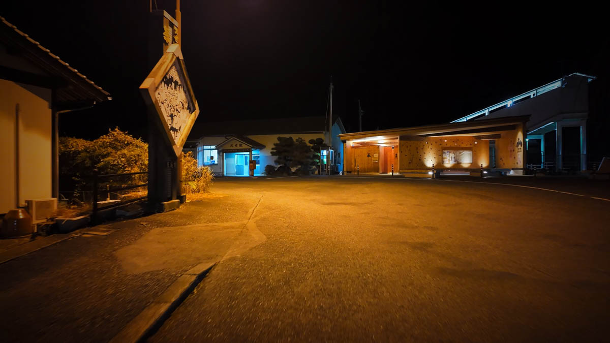 The plaza in front of Kuse Station at night, with a carved wooden sign on the left and a wooden public facility on the right