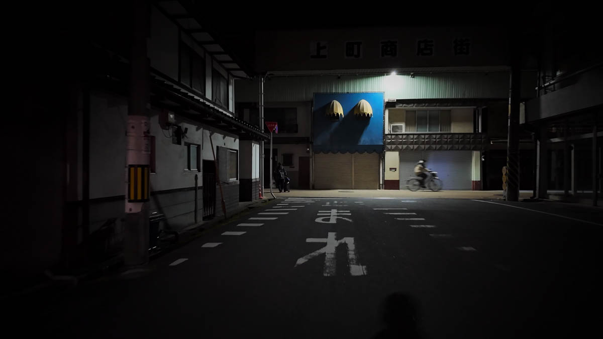 Entrance to Kamimachi Shopping Street, with a large blue sign and a cyclist passing by