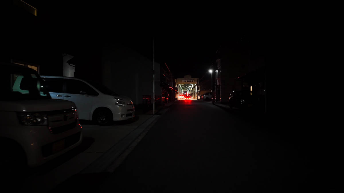 A dark side street with the roof of Kamimachi Shopping Street visible in the distance