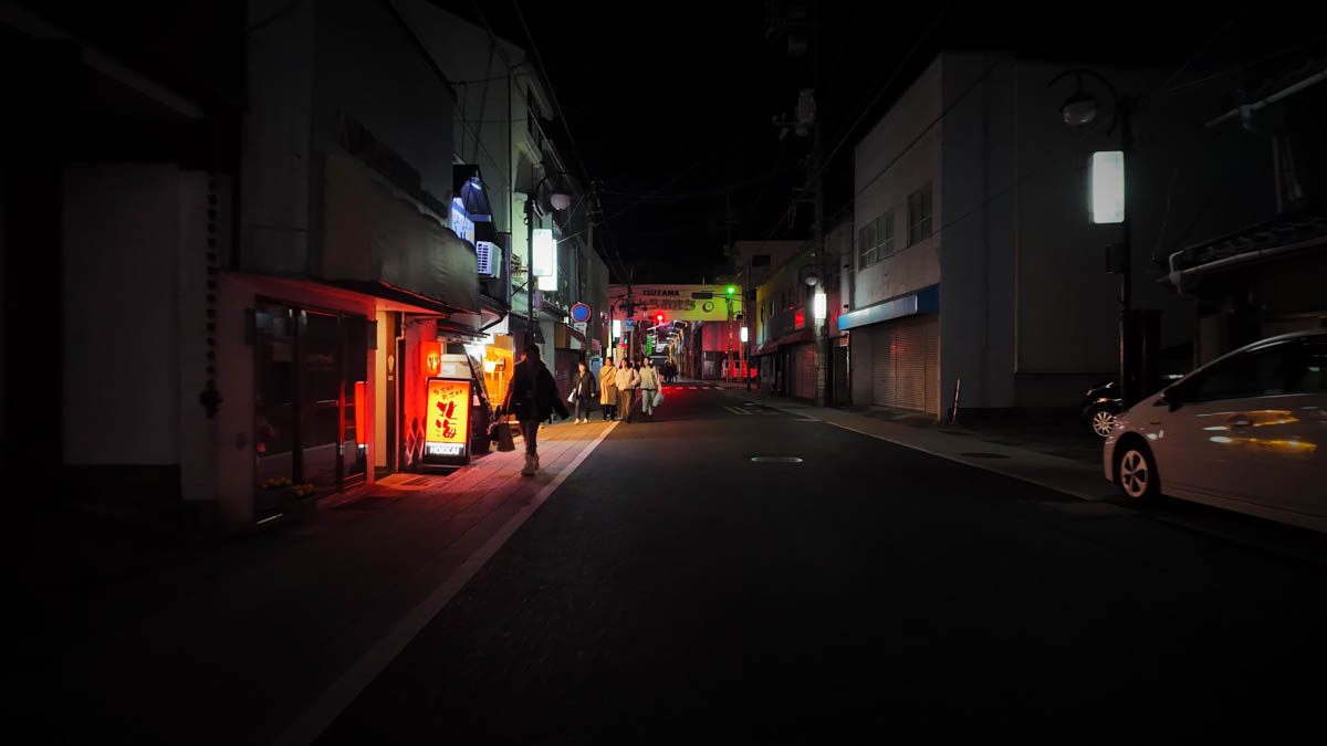 A drinking street in Tsuyama, with a red-lit restaurant sign and a group walking down the road