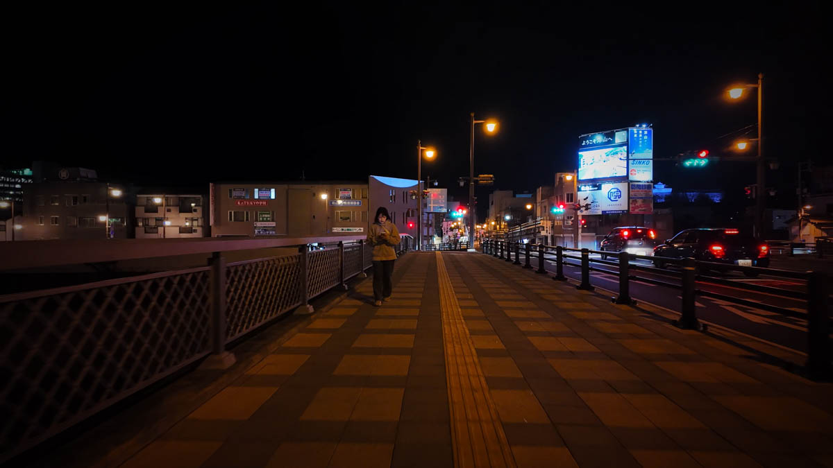 The sidewalk of Imazuyabashi Bridge at night, with railings along the Yoshii River and city lights ahead