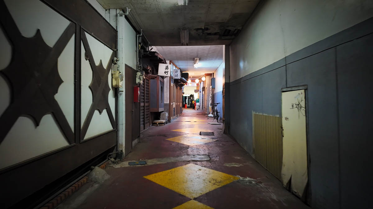A narrow passage running through a building, with izakaya signs and lights continuing into the distance