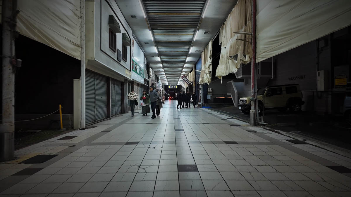A covered shopping arcade in Tsuyama, with a small group walking past closed storefronts