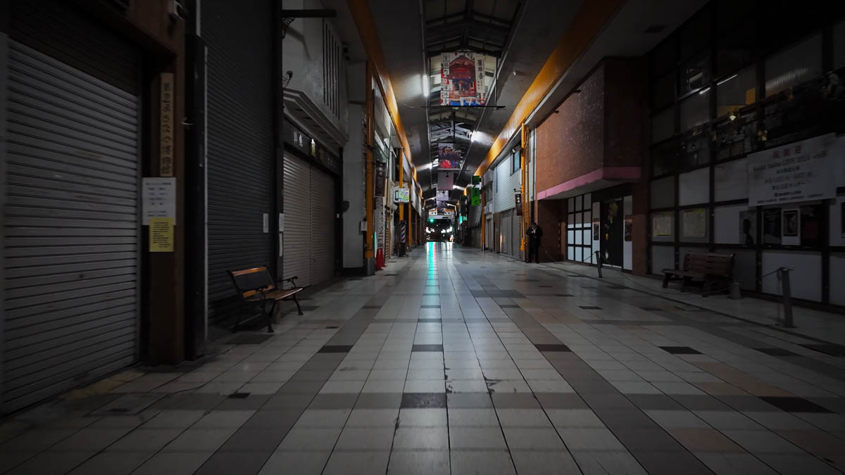 A quiet covered arcade at night, with closed shutters and benches lining the walkway