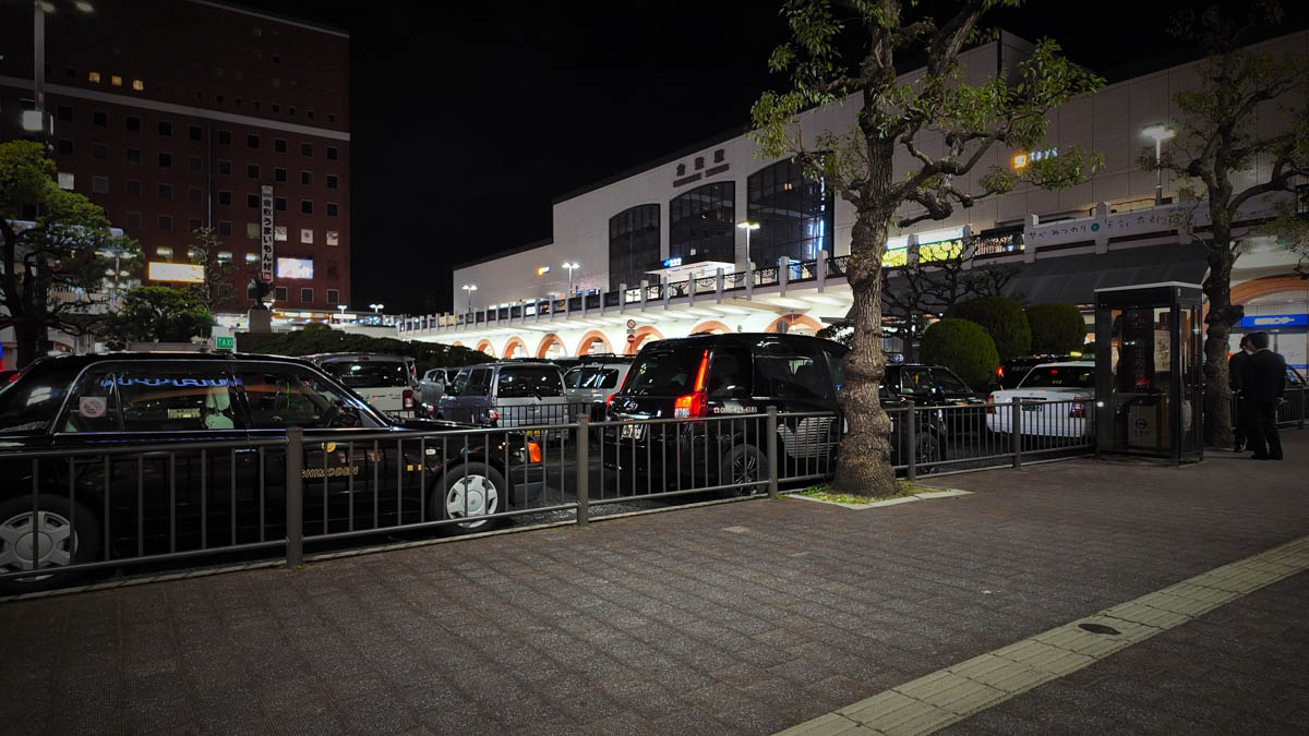 Taxis lined up in front of Kurashiki Station at night, with the arched station building glowing in the background