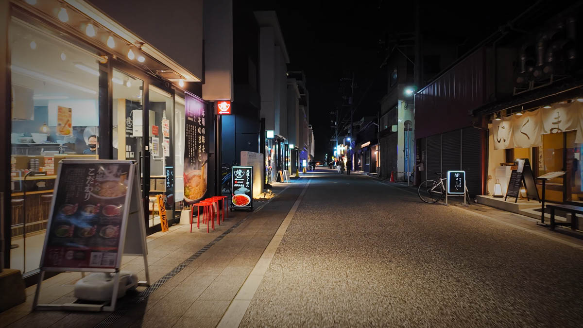 A restaurant street at night, with a red niboshi ramen sign and a Japanese restaurant visible