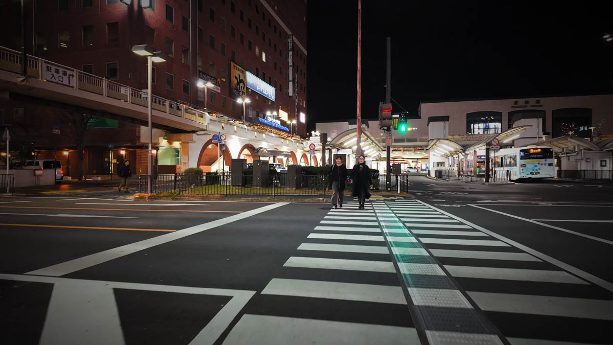 The intersection in front of Kurashiki Station at night, with a red-brick hotel building on the left and the arched station building in the distance