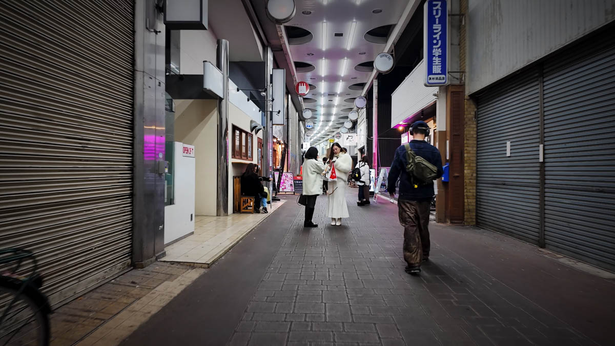 A covered arcade at night, with several people standing near closed shutters