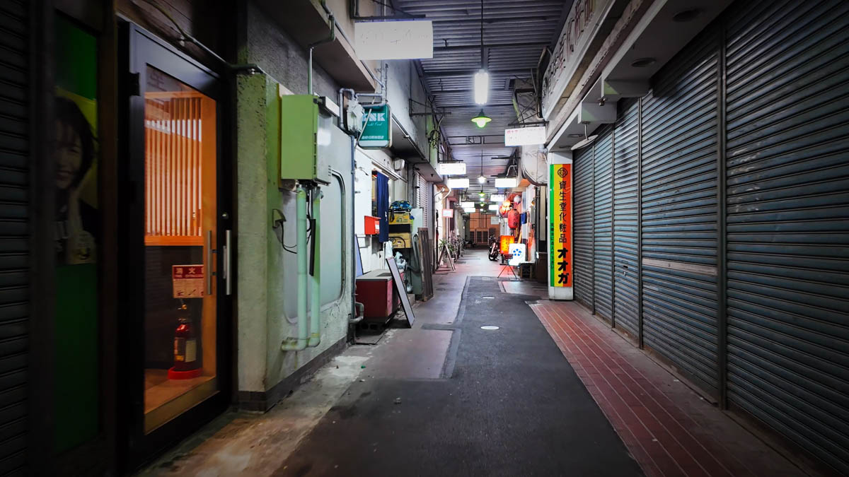 A side passage with closed shutters and faint lights farther inside
