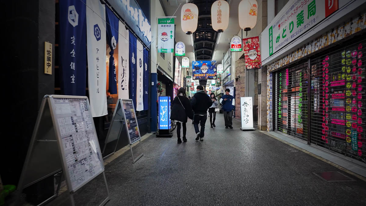 A covered arcade near the Bikan Historical Quarter, with a sign pointing toward the historic district, Christmas decorations, and restaurant curtains