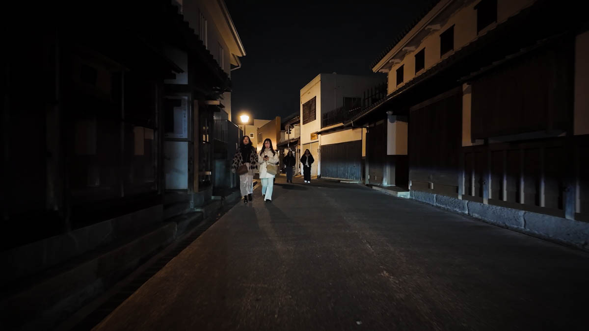 A night street in the Bikan Historical Quarter, with traditional buildings, lattice windows, and people walking through the scene