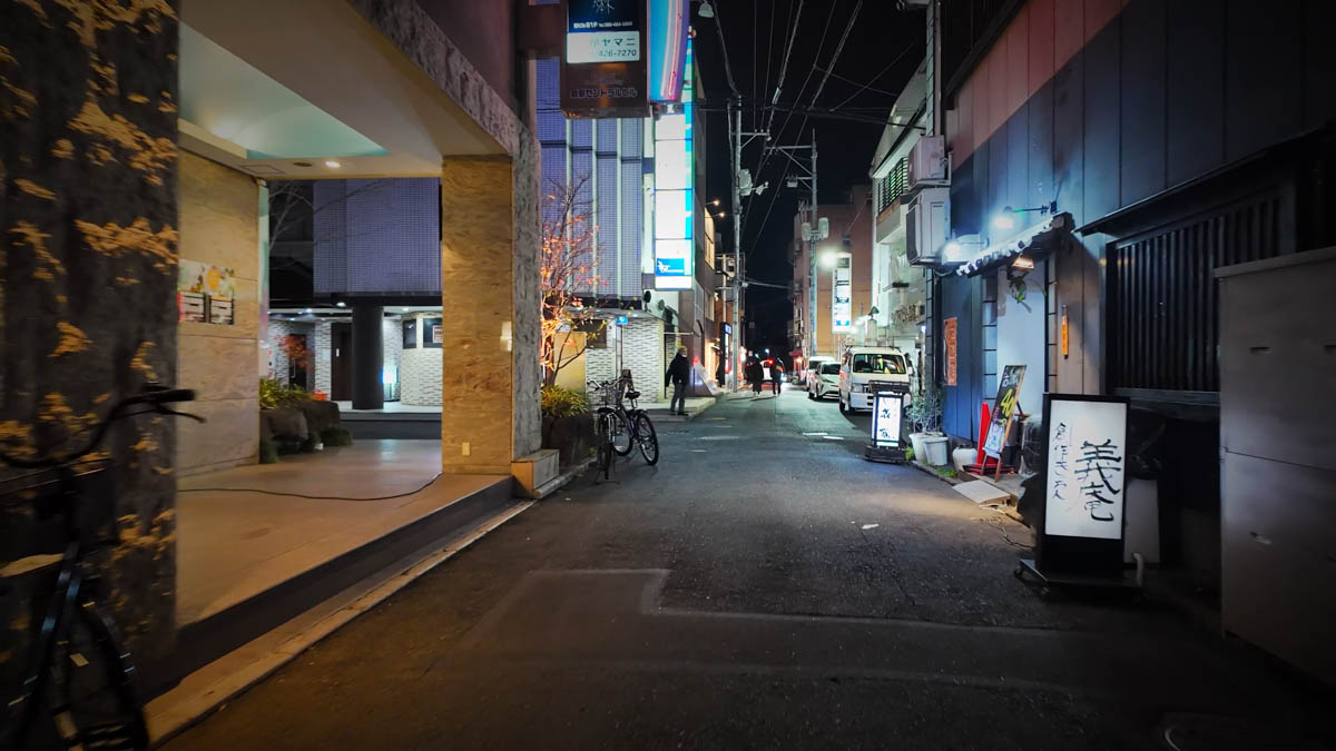 A night side street near the Bikan Historical Quarter, lined with older buildings and restaurant signs