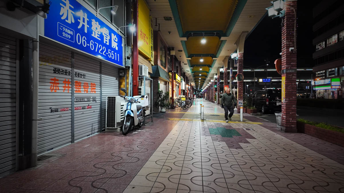 A covered walkway near Fuse Station at night, with a chiropractic clinic sign and tiled floor, and station lights visible in the distance