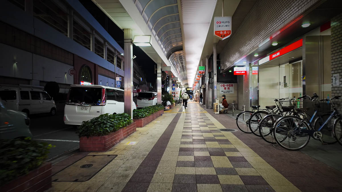 A covered sidewalk in front of Fuse Station, with bank signs, bicycle parking, and the road stretching ahead