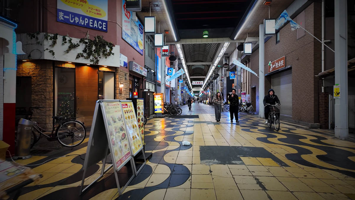 Inside the Fuse covered shopping arcade, with a yellow-and-black patterned floor, restaurant signs, and a person cycling through