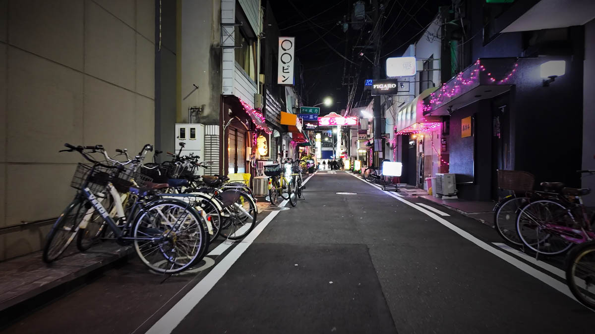 A narrow alley in Fuse's restaurant district, with bicycles parked along the side and bar and snack signs continuing into the distance