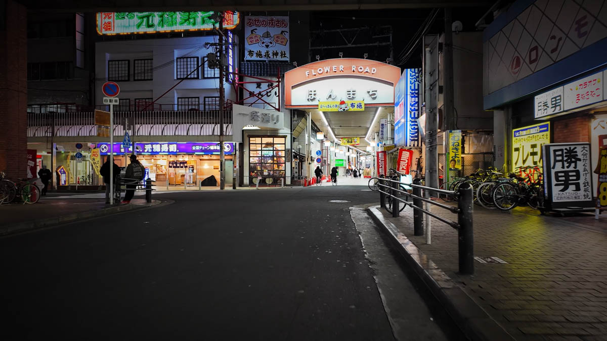 The entrance to Flower Road Honmachi in Fuse, surrounded by a drugstore and shopping arcade signs