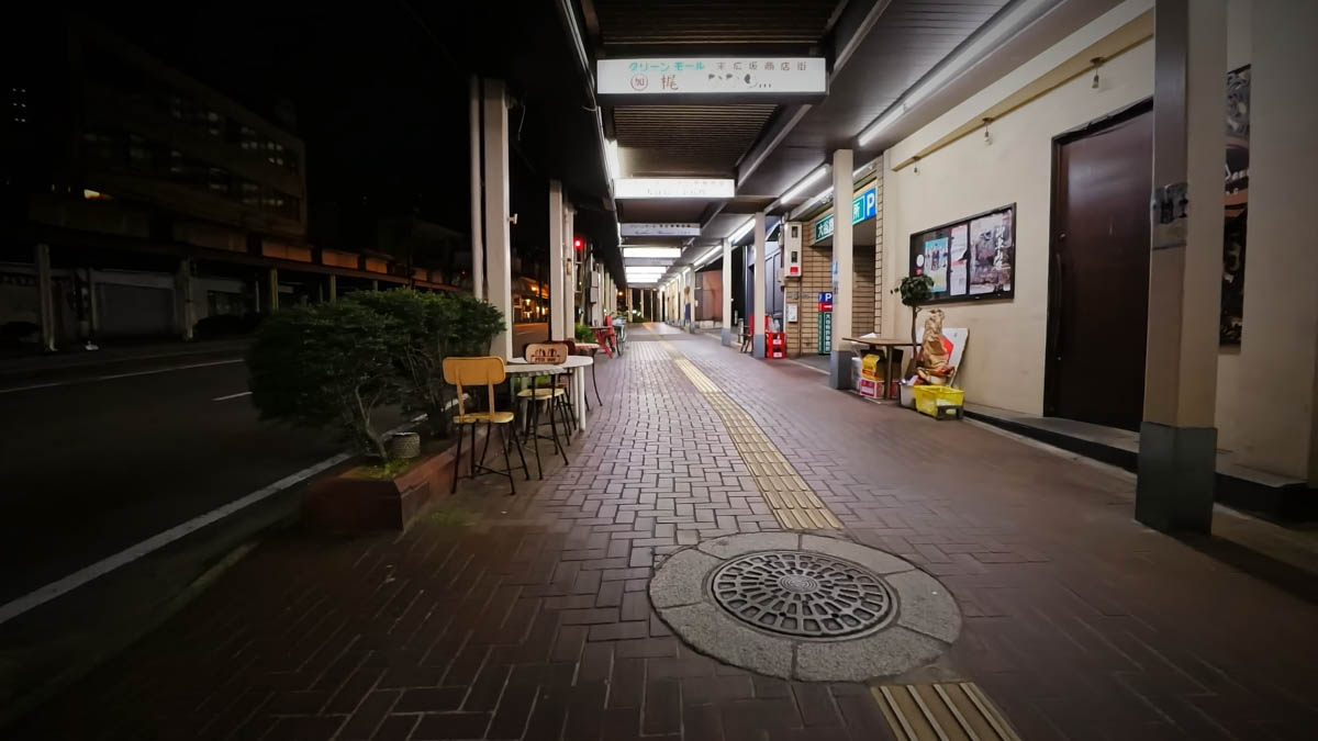Green Mall Suehiro shopping street at night, with the passage lights on and a table and chairs set out in front of one shop