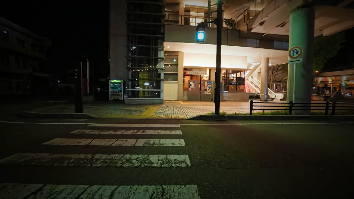A late-night street in front of Takaoka Station, with a pedestrian crossing leading toward an elevated structure