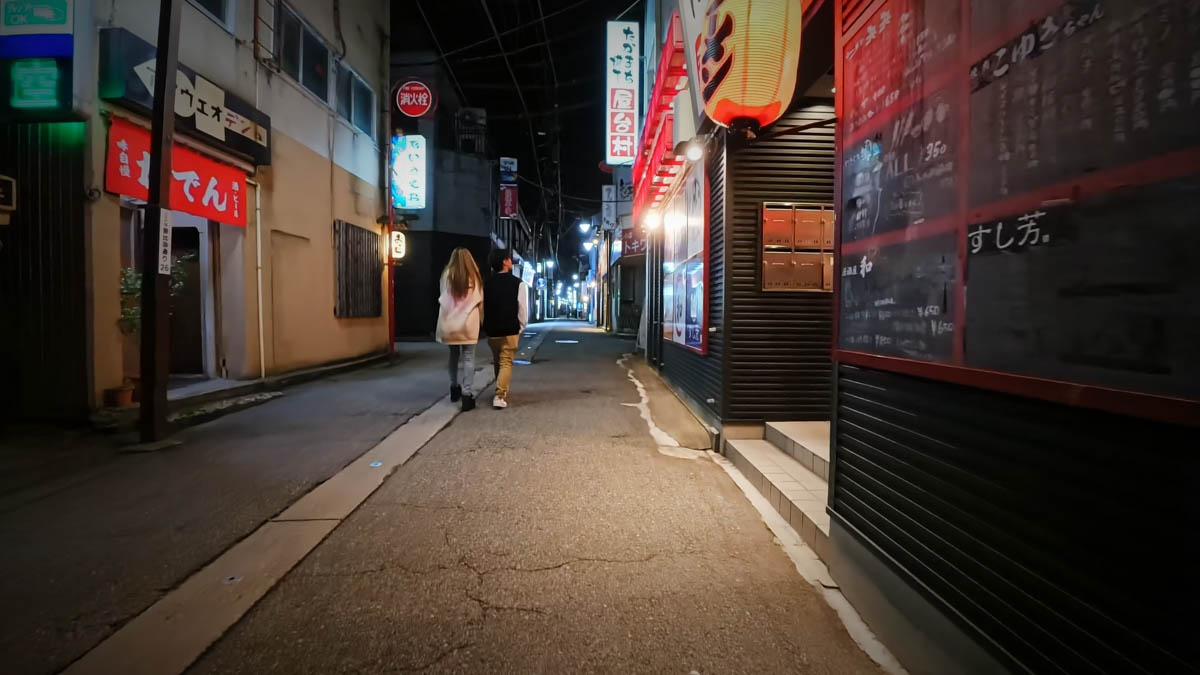 A restaurant alley with signs for Den, Sushiyoshi, Koyuki, and others. A couple walks away down the passage