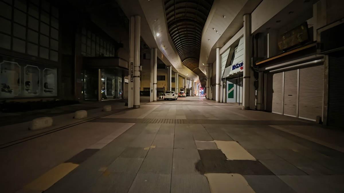 Inside a covered shopping arcade at night. The wide passage is empty except for a single car visible in the distance