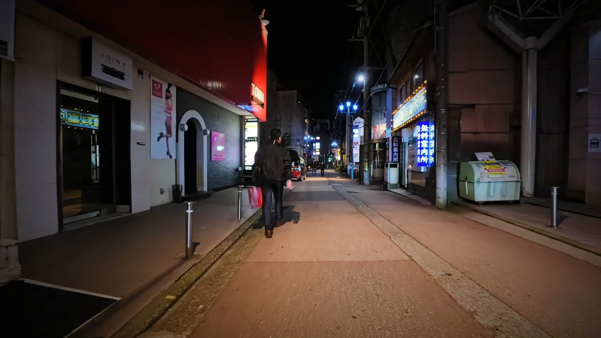 A street in the entertainment district with a JOINT sign, a "free information booth" visible, and one man walking