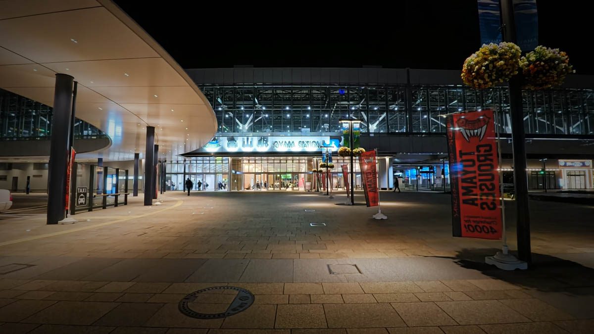 夜の富山駅正面。ガラス張りの駅舎と駅前広場、バナーが並ぶ