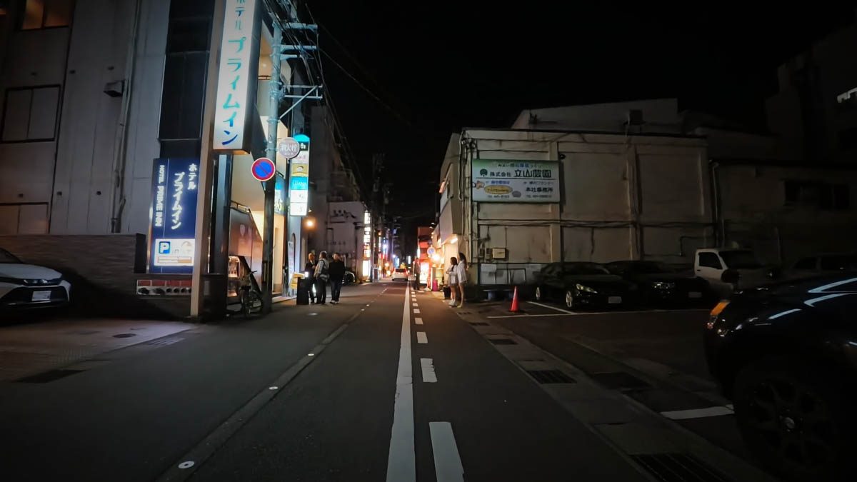 ホテルプライムイン富山近くの通り。ホテルの縦看板と駐車場、奥の飲食店街が見える