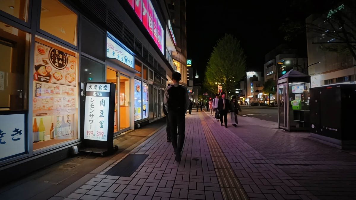 富山駅近くの歩道。飲食店の看板と通行人、街路樹が見える