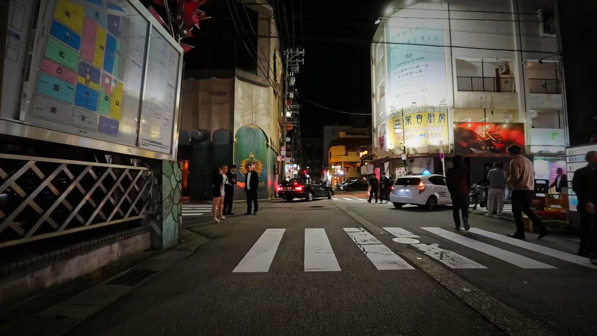 富山駅近くの夜の路地。案内看板と飲食店の明かり、横断歩道が見える