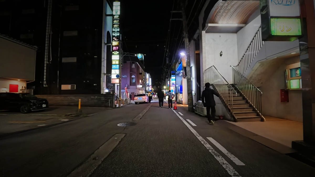 富山駅近くの飲食店街。ビルの階段と縦看板、路地を歩く人が見える