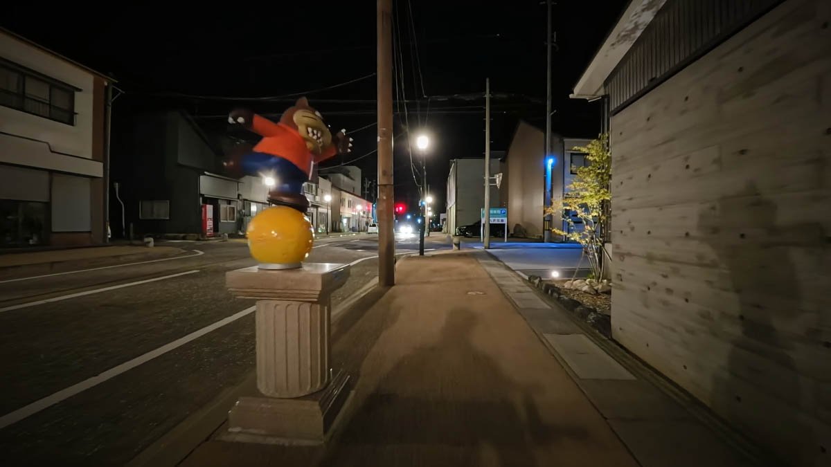夜の通り。台座に立つオオカミ男（変身後）の像。奥に木造の建物が見える