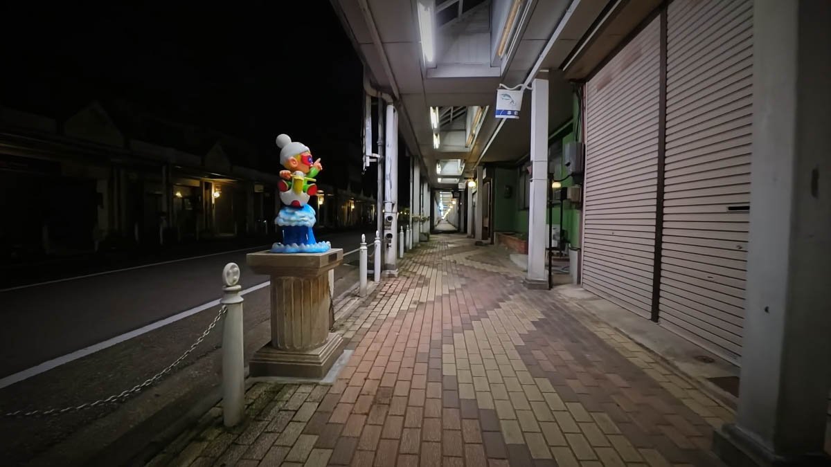 夜のアーケード入口。ウルトラBのUB（ユービー）の像が台座に立ち、奥にシャッターの閉まった商店街が続く