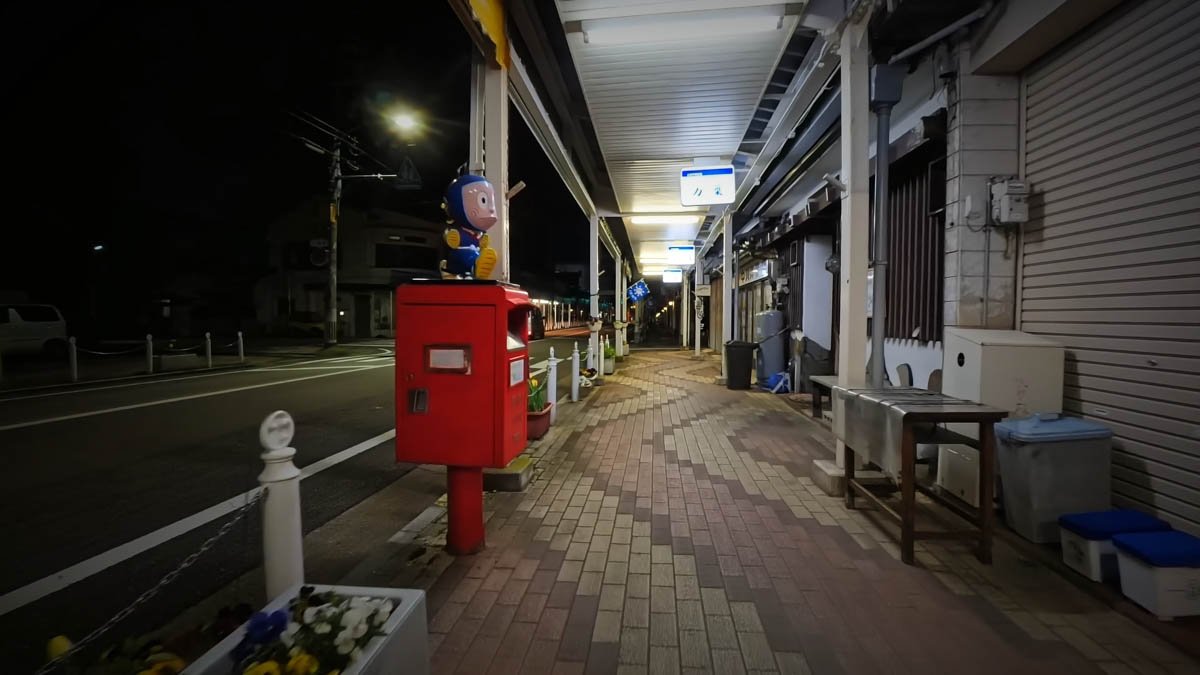 夜のアーケード商店街。赤いポストの上に忍者ハットリくんのハットリくんの像が乗り、奥にアーケードが続く