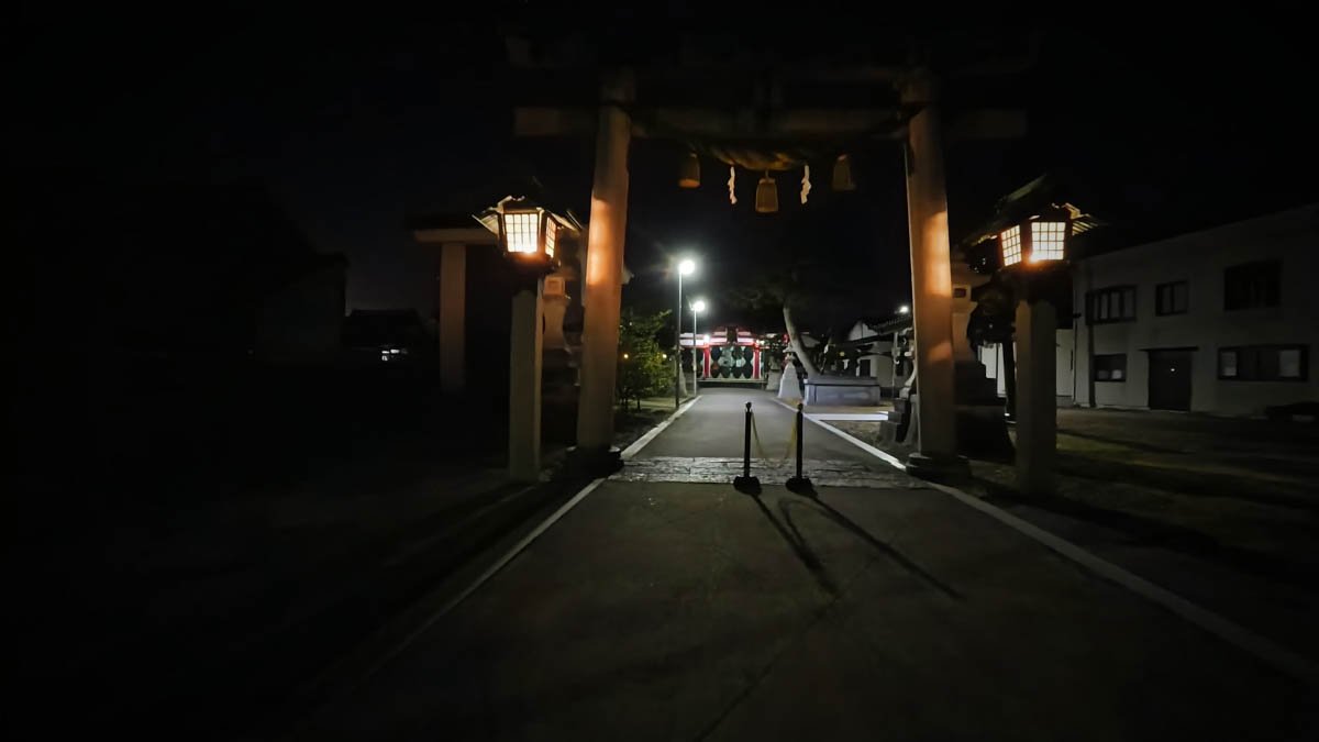 夜の日宮神社の鳥居。両脇に灯籠が灯り、奥に赤い社殿が見える
