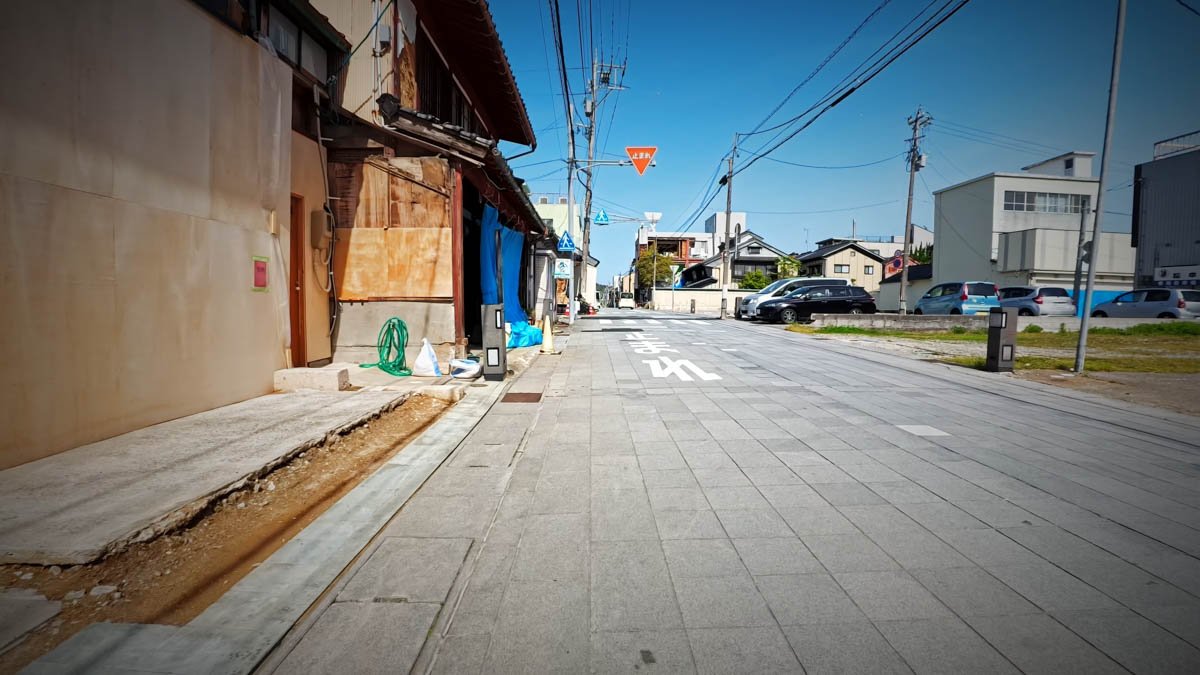 七尾市内 ブルーシートと復旧工事 新しく舗装された歩道の左に、合板で補修された建物が続く。基礎はひび割れ、奥にはブルーシートに覆われた建物も見える