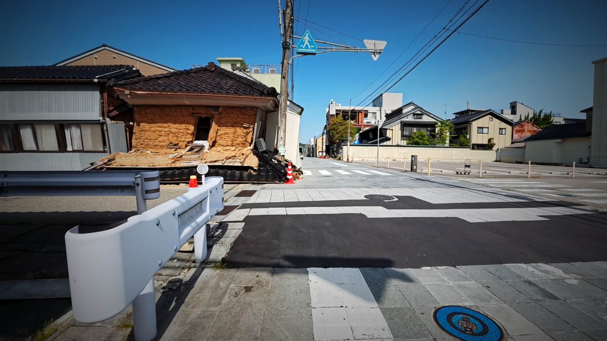 七尾市内 倒壊した建物 交差点の角に建物が完全に倒壊している。土壁が崩れ落ち、屋根瓦が路上に散乱。周囲にコーンが置かれている