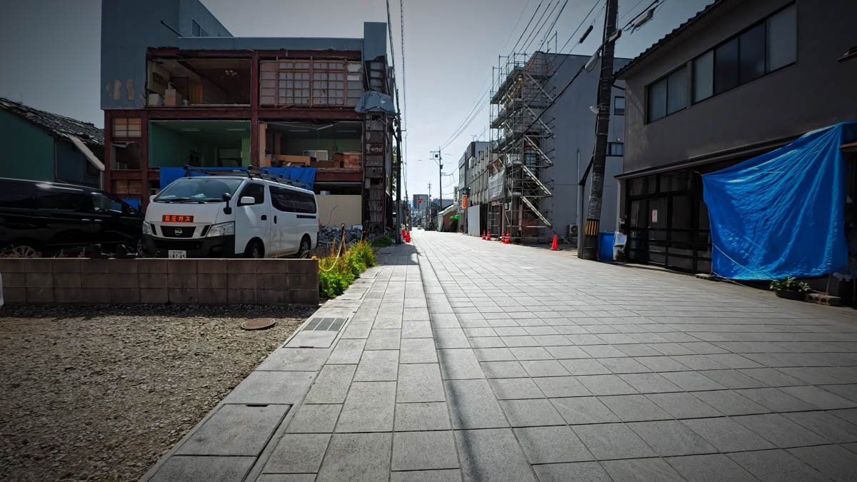 七尾 一本杉通り 建物内部が露出した家屋と足場 一本杉通りの一角。左手に壁がはがれ内部が剥き出しになった建物。右手にはブルーシートと足場が組まれ、「高圧ガス」と書かれた車が停まっている